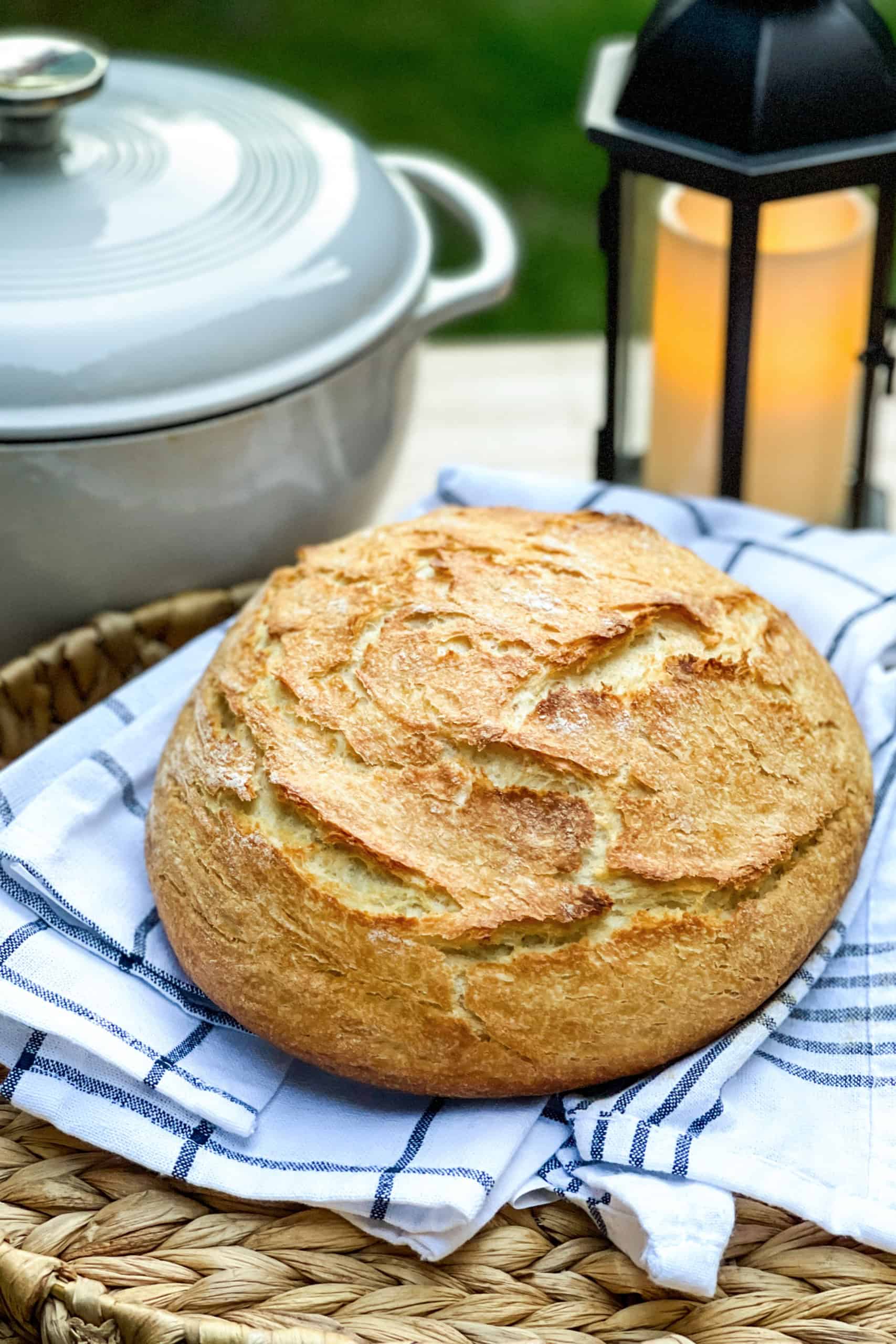 Unsliced Dutch Oven Camp Bread with a golden crust in a basket near a lantern and a Dutch Oven.