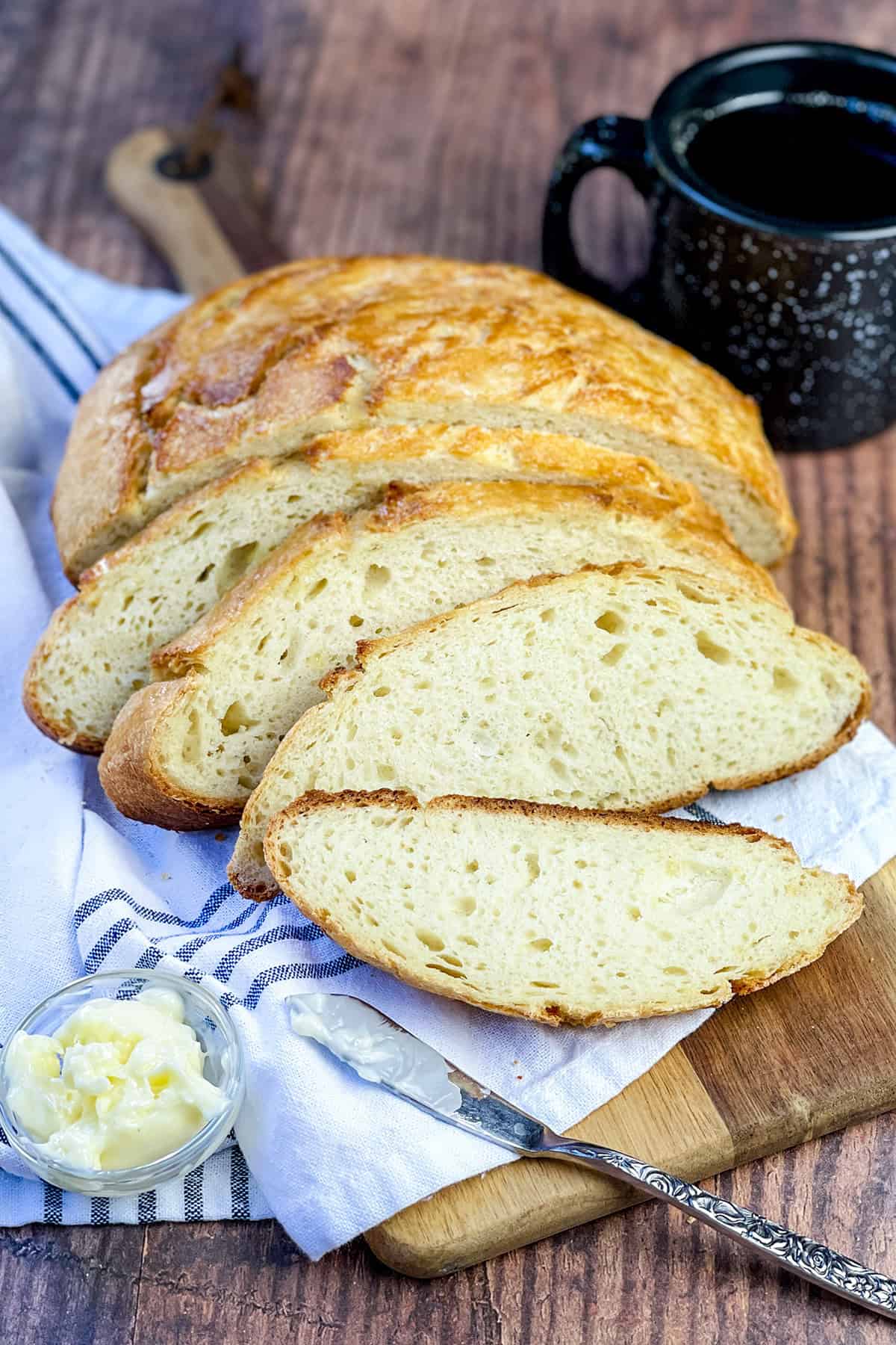 Sliced dutch oven camp bread with a golden crust ready for serving on a linen lined wooden serving board.