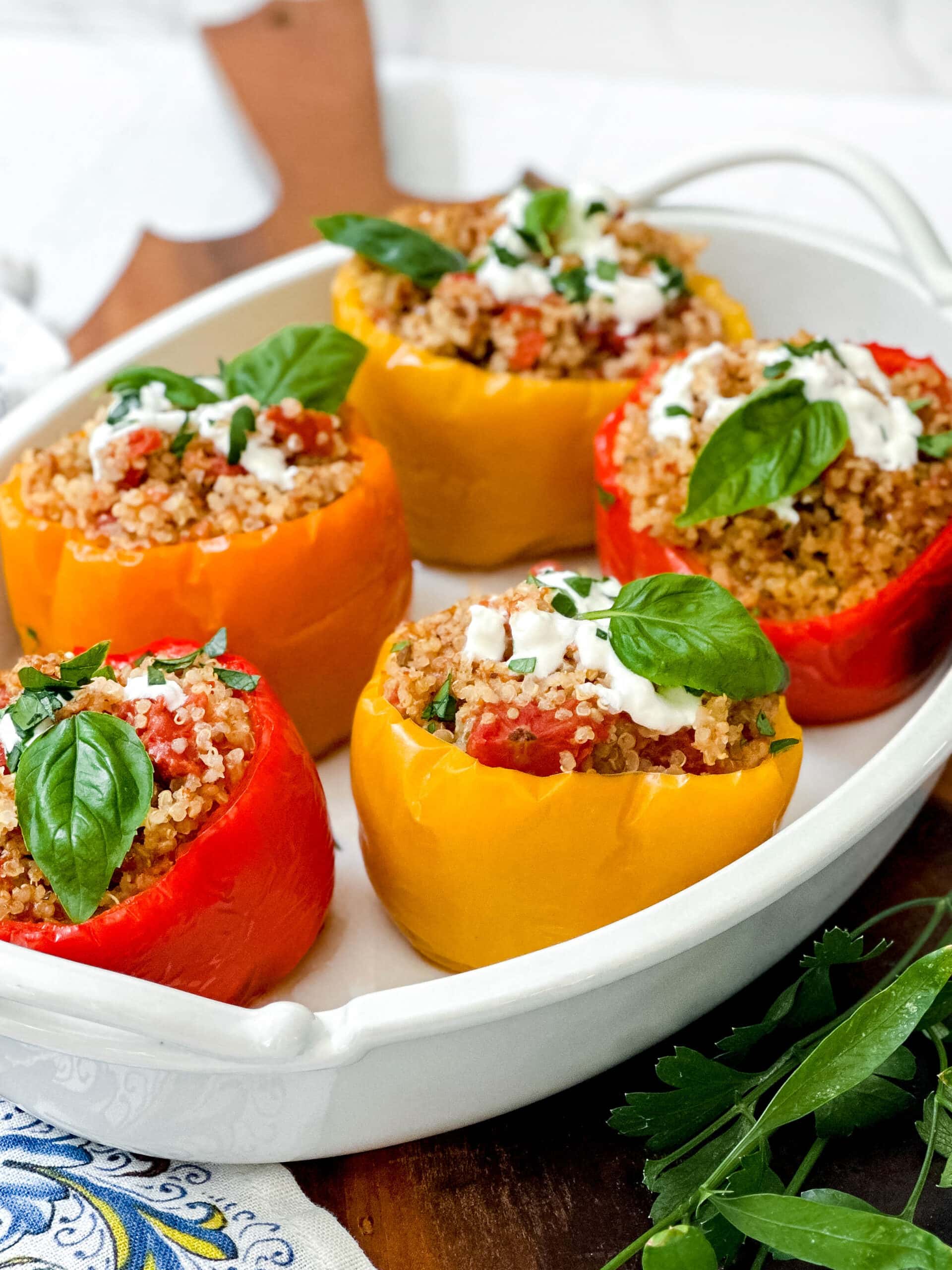 Closeup side view of Crockpot Stuffed Peppers in a white oval serving dish with fresh basil and Greek yogurt.