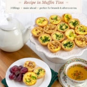 Mini Quiche varieties with delicious fillings are artfully arranged on a white platter alongside a white teapot, a cup of tea, and a plate featuring more mini quiches and grapes atop a wooden tray.