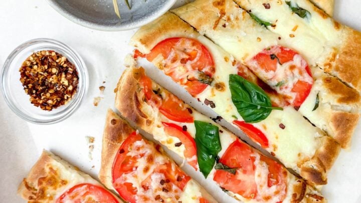 Top view of sliced grilled flatbread with tomatoes, torn basil and mozzarella cheese.