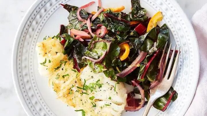 A plate of cooked white fish garnished with herbs, served alongside saut&eacute;ed Swiss chard and bell peppers, makes for a perfect August Mediterranean dinner&mdash;completed with a fork on the plate.