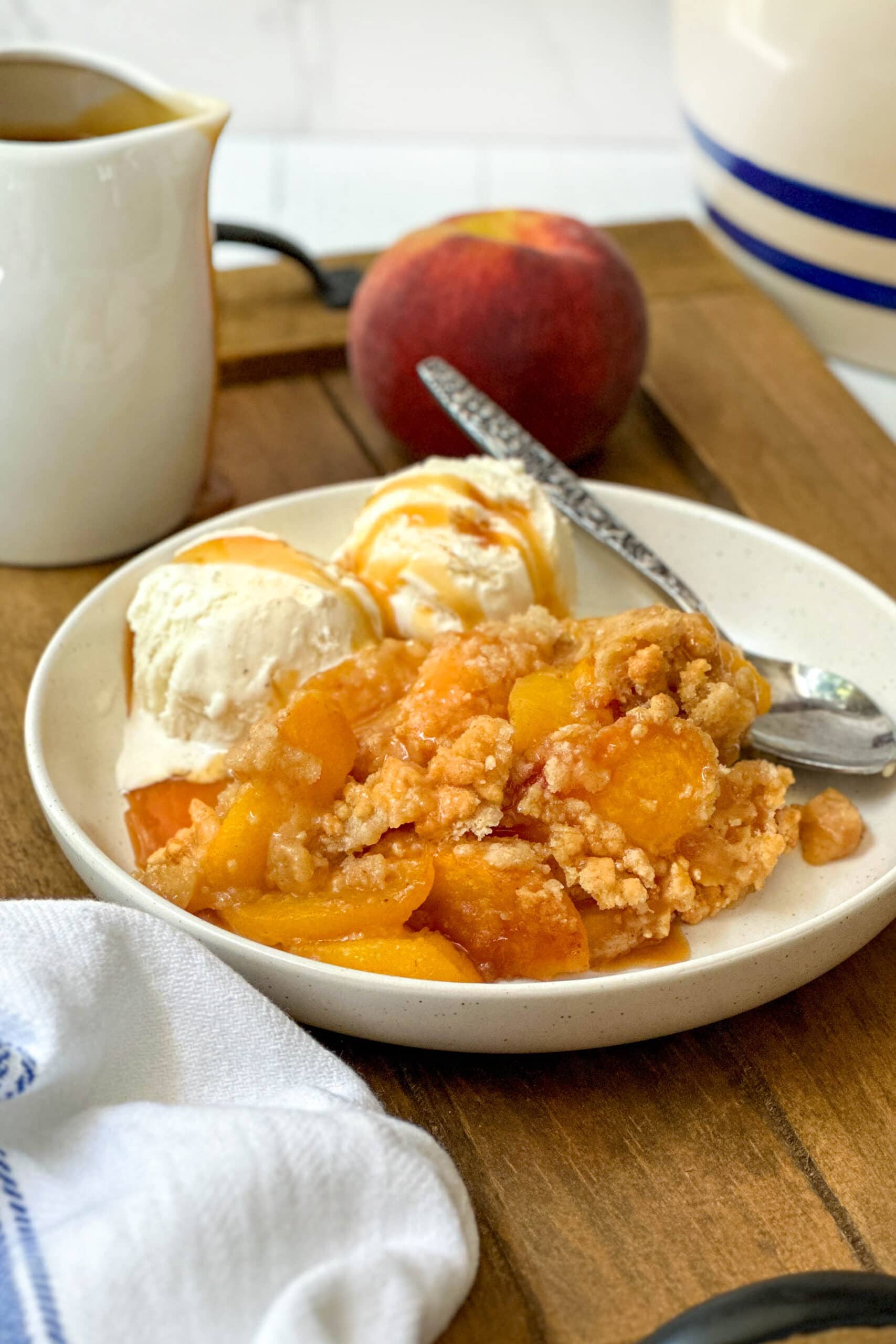 Side view of peach crumble with melting vanilla ice cream and caramel sauce in a white bowl.