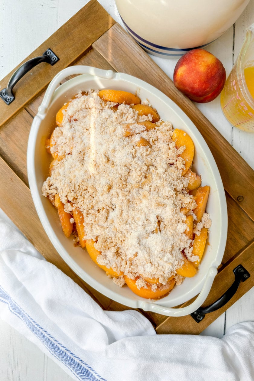 Top view of unbaked Peach Crumble in an oval white baking dish with topping