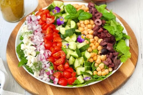 Top side view of Mediterranean Chopped Salad in a white serving bowl on a round wood board