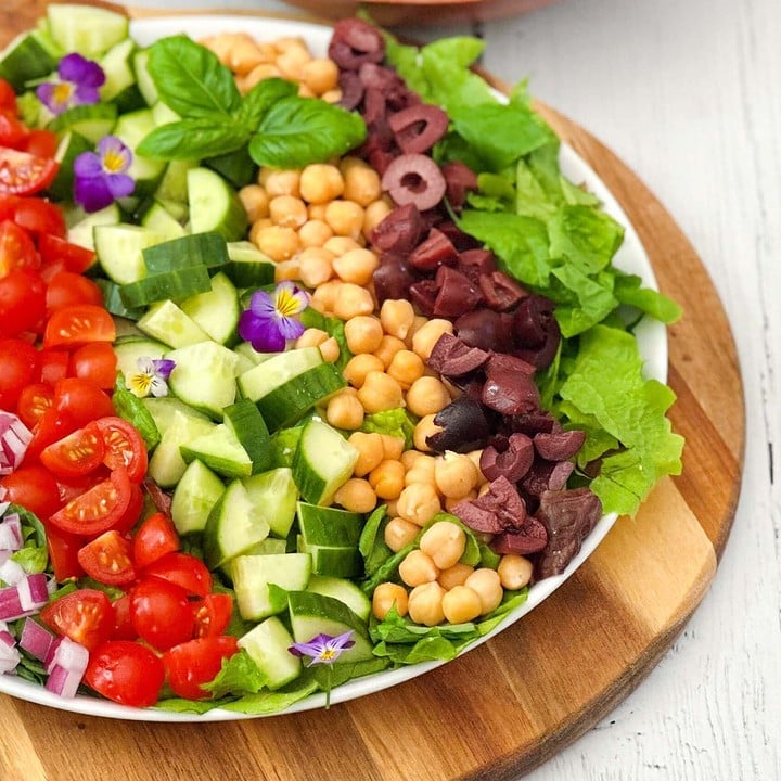 Top side view of Mediterranean Chopped Salad in a white serving bowl on a round wood board