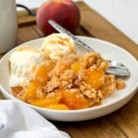 Side view of warm from the oven peach crumble with vanilla ice cream and salted caramel sauce over the top.