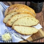 Sliced Dutch Oven Camp Bread on a wooden cutting board with a blue and white towel.