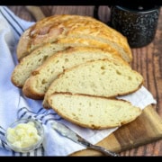 Sliced Dutch Oven Camp Bread on a wooden cutting board with a blue and white towel.