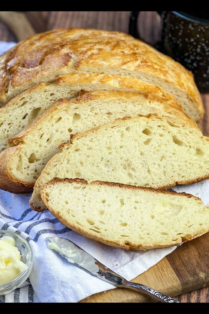 Sliced Dutch Oven Camp Bread on a wooden cutting board with a blue and white towel.