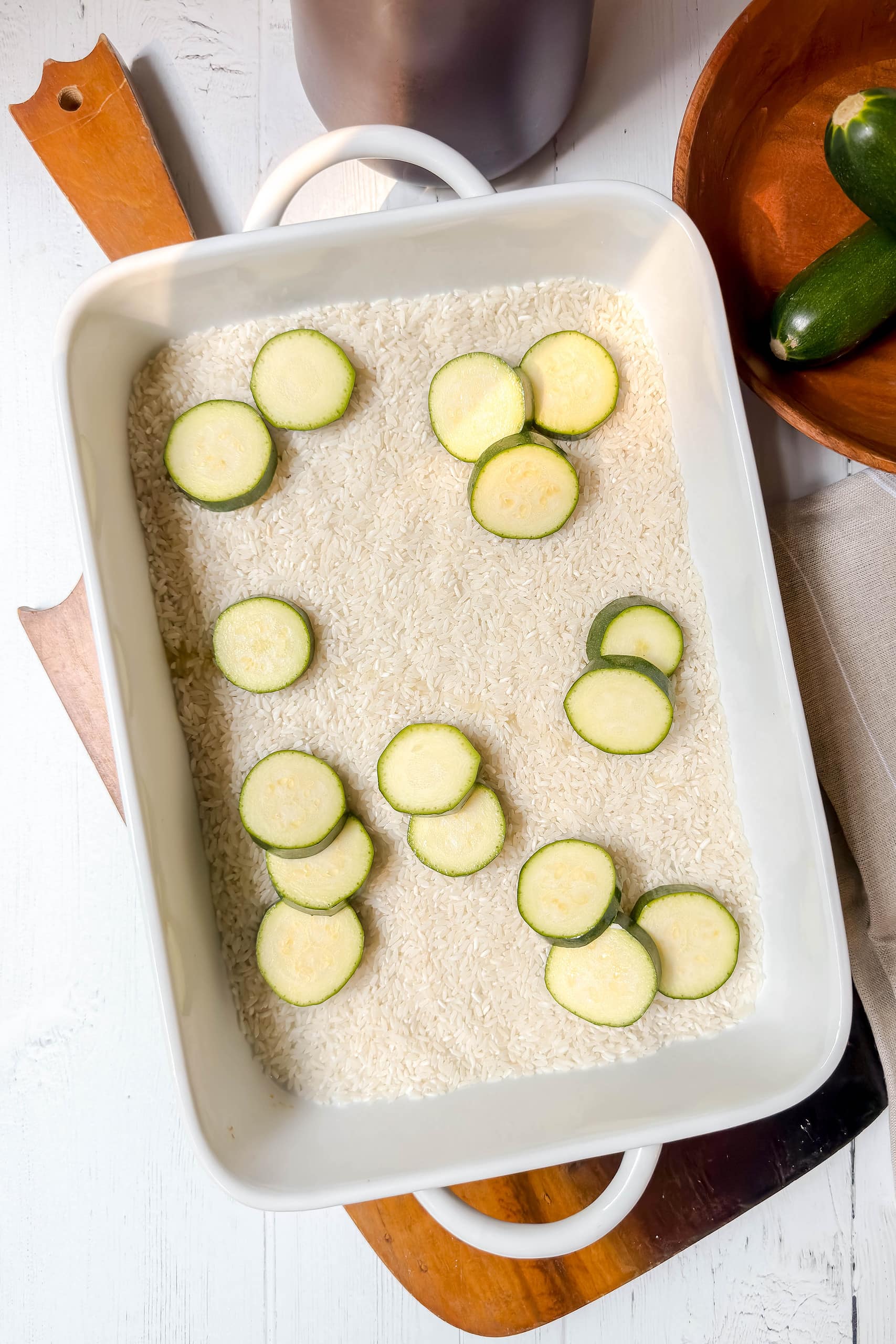 Top view of dry rice and sliced zucchini in a casserole dish