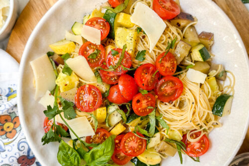 Top view of Garden Pasta with vegetables, cherry tomatoes, and fresh basil in a white pasta plate