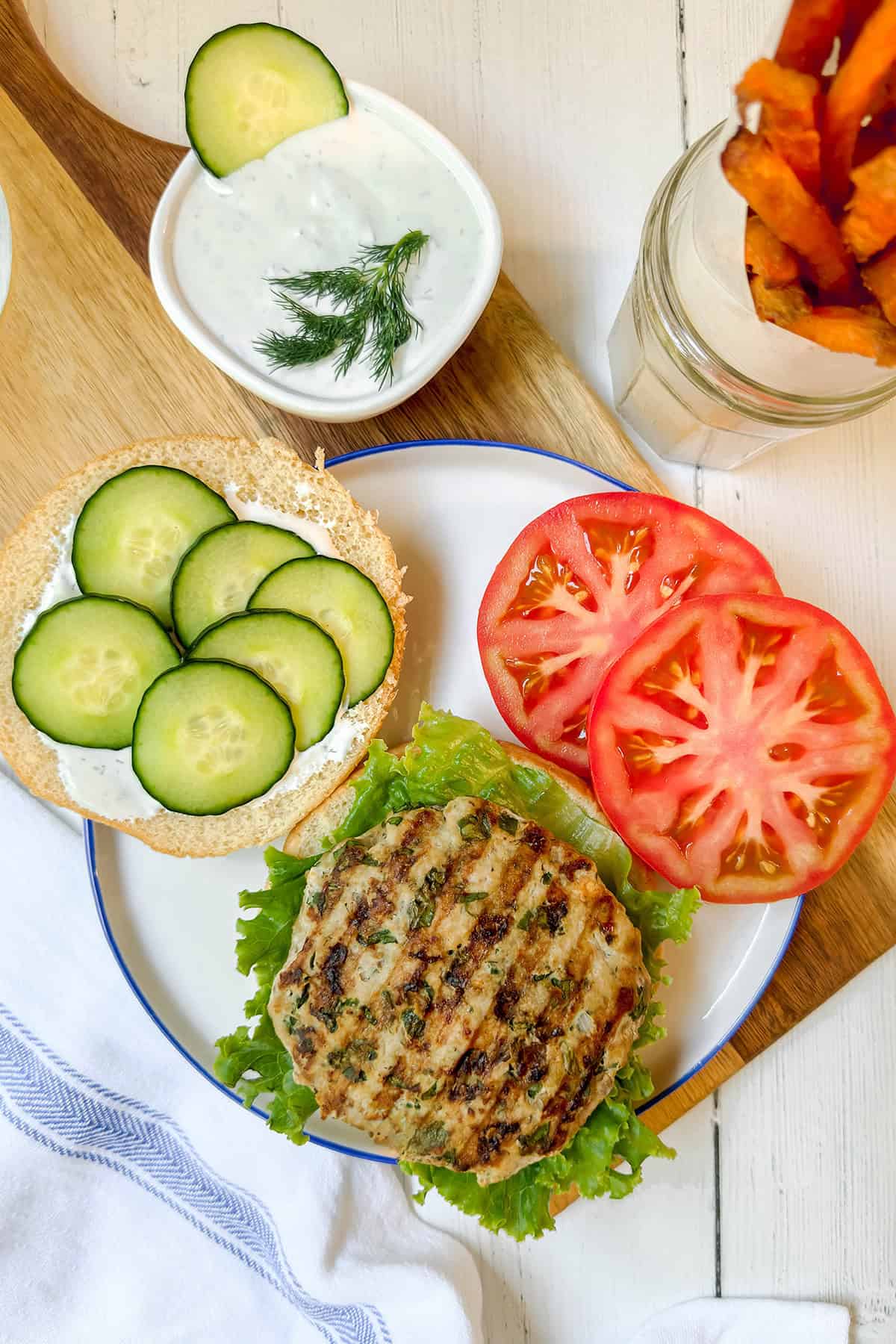 Greek turkey burger on a bun with cucumber slices, tomato, lettuce, and tzatziki sauce. 