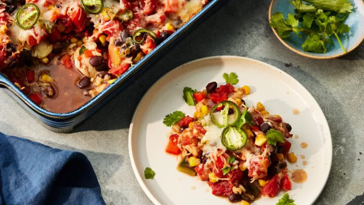 A serving of colorful Mexican casserole with beans, corn, tomatoes, cheese, and jalapeño slices sits on a white plate—an ideal choice for Late Summer DASH Diet Dinners—beside a baking dish and a small plate of cilantro.