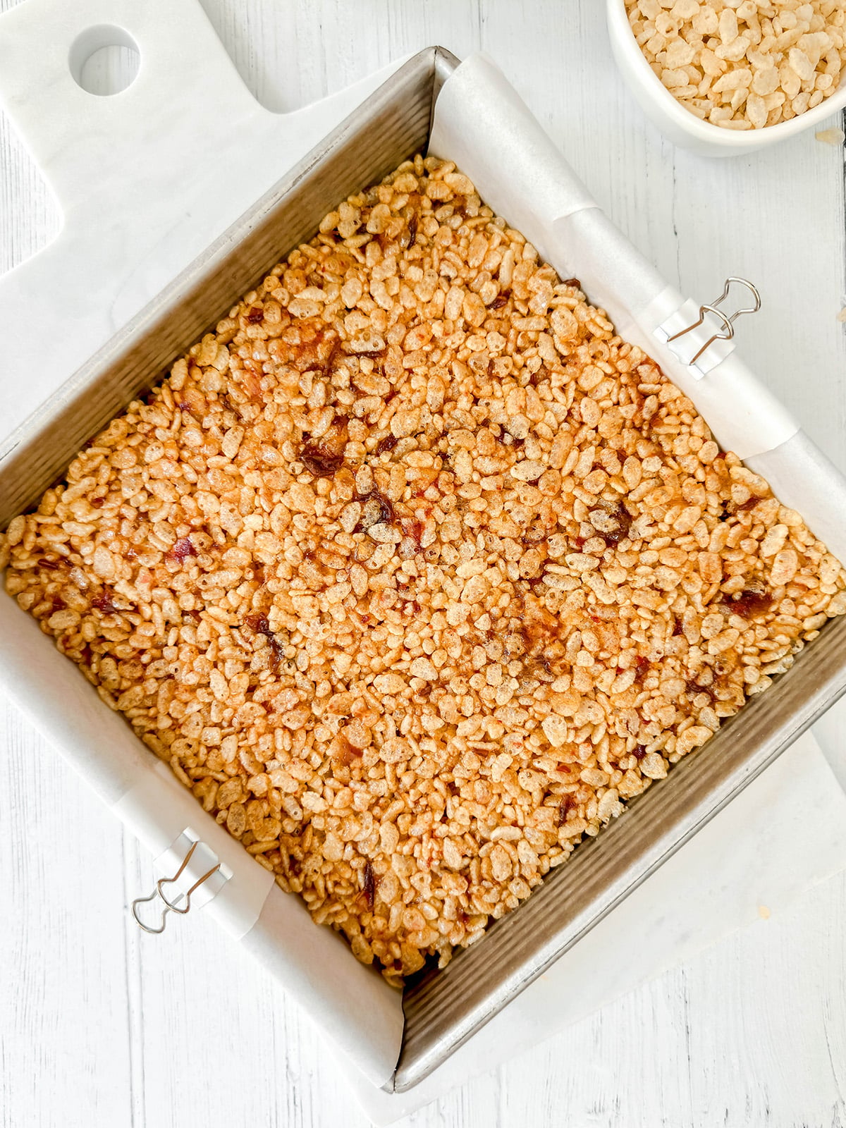 Rice Bubble Slice mixture pressed into a parchment-lined square pan to cool.