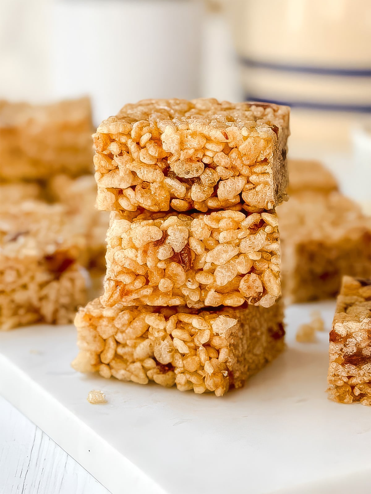 Three Rice Bubble Slice squares stacked on a white surface with more pieces blurred in the background