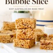 Stacked Rice Bubble Slice bars on a white board, surrounded by more bars, with a bowl and blue-striped plate in the background. Text at top describes the treat as an Australian no-bake dessert.