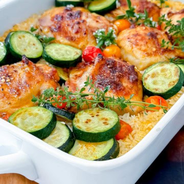 Baked chicken and rice with zucchini slices, cherry tomatoes, and fresh thyme in a white casserole dish.