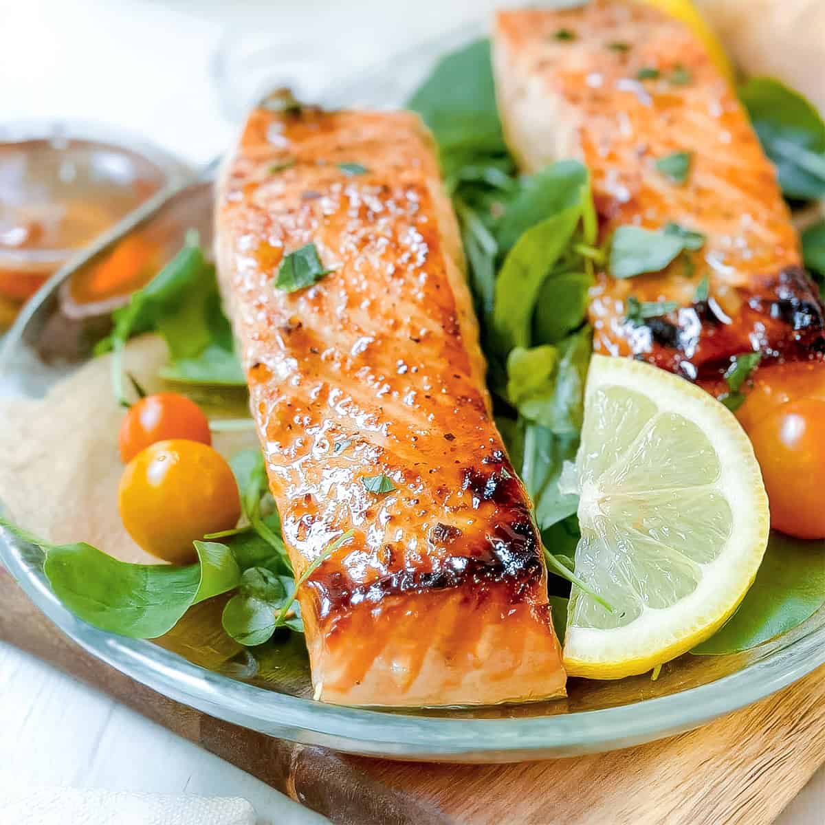 Grilled salmon fillets served on a bed of fresh greens with cherry tomatoes and lemon slices on a glass plate-an irresistible salmon recipe for any occasion.