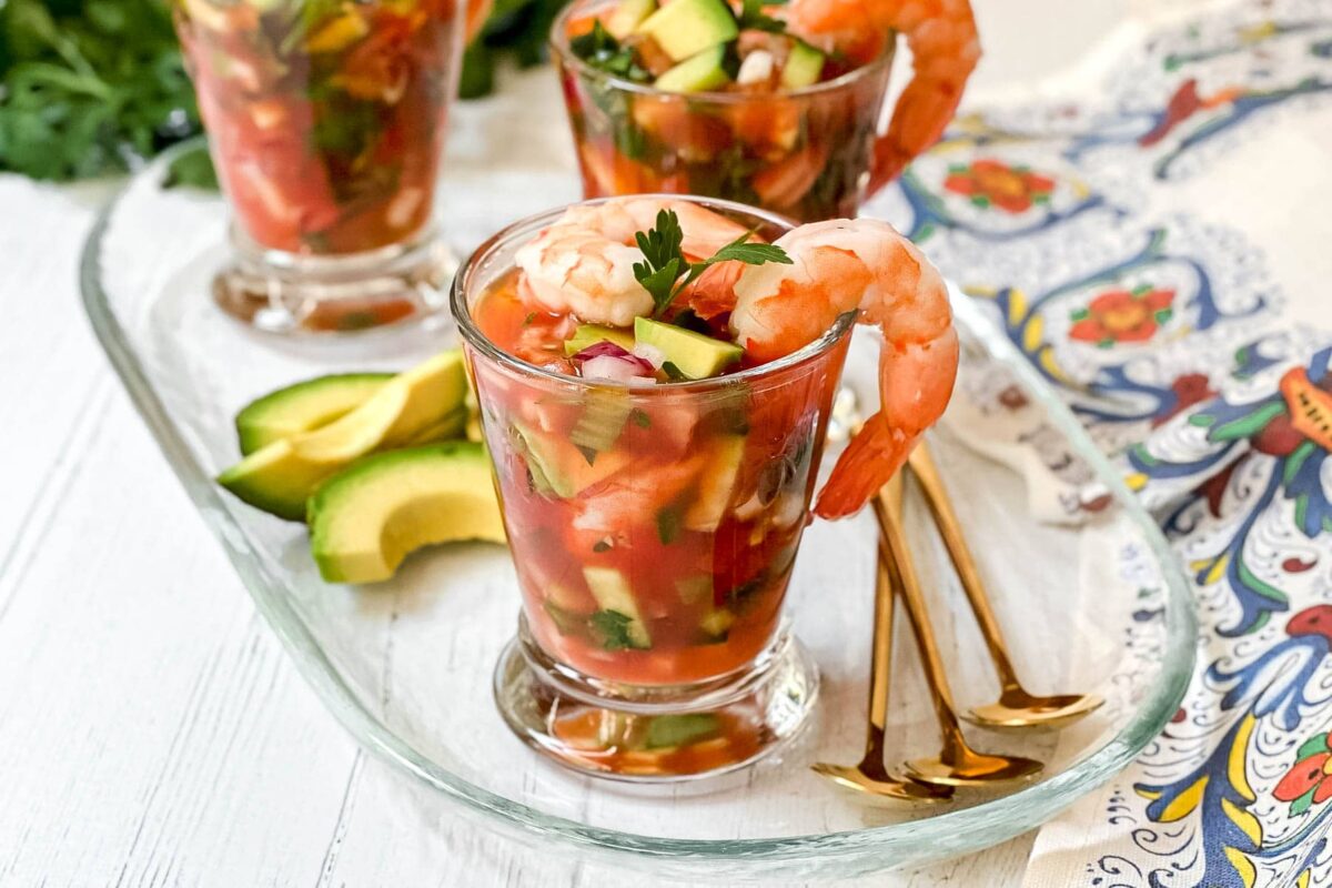 Side view of Mexican Shrimp Cocktail on a glass serving tray for guests with wedges of avocado and fresh cilantro