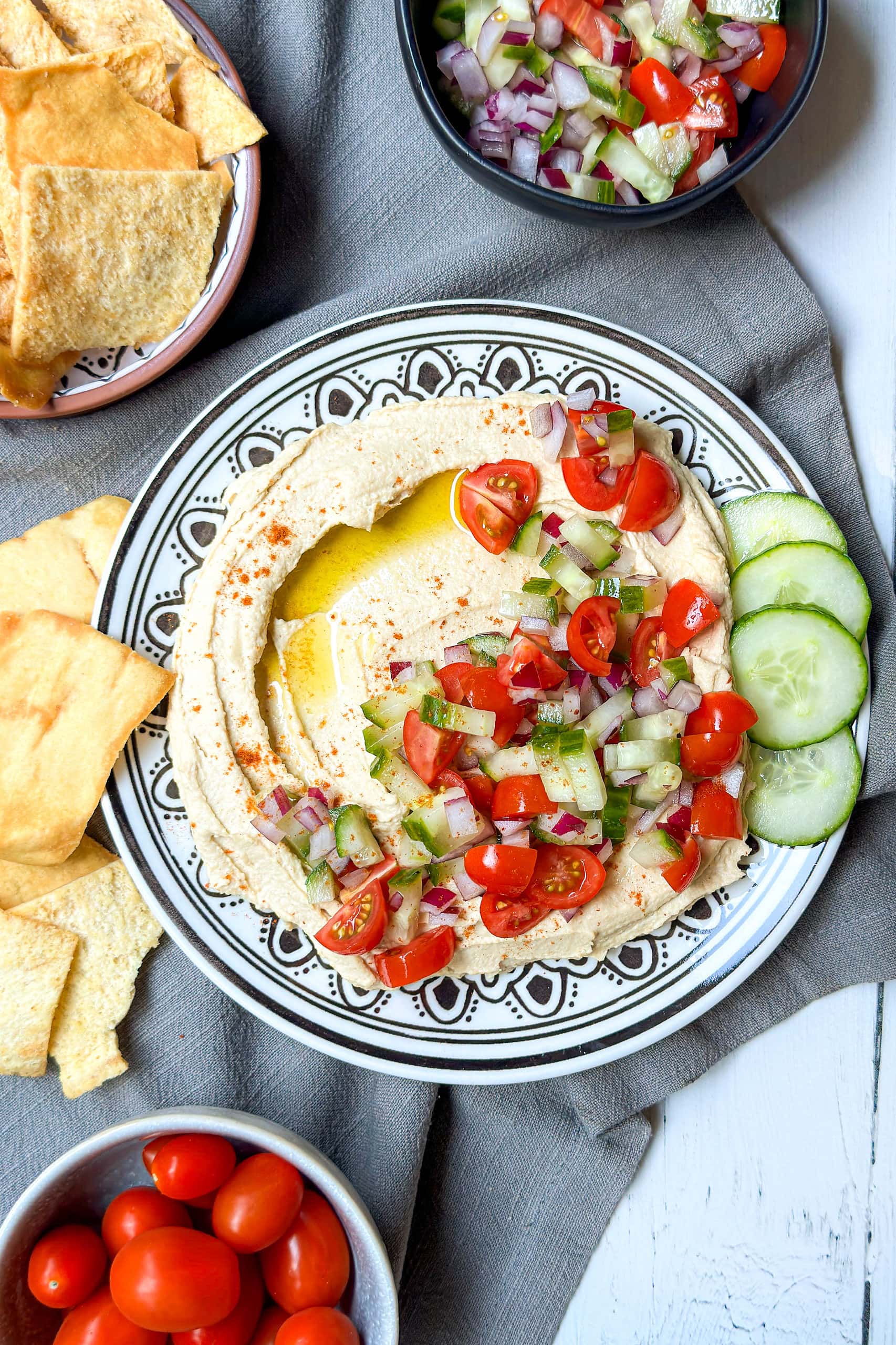 Top view of Hummus on a black and white plate with olive oil, cherry tomatoes, cucumbers, and red onion