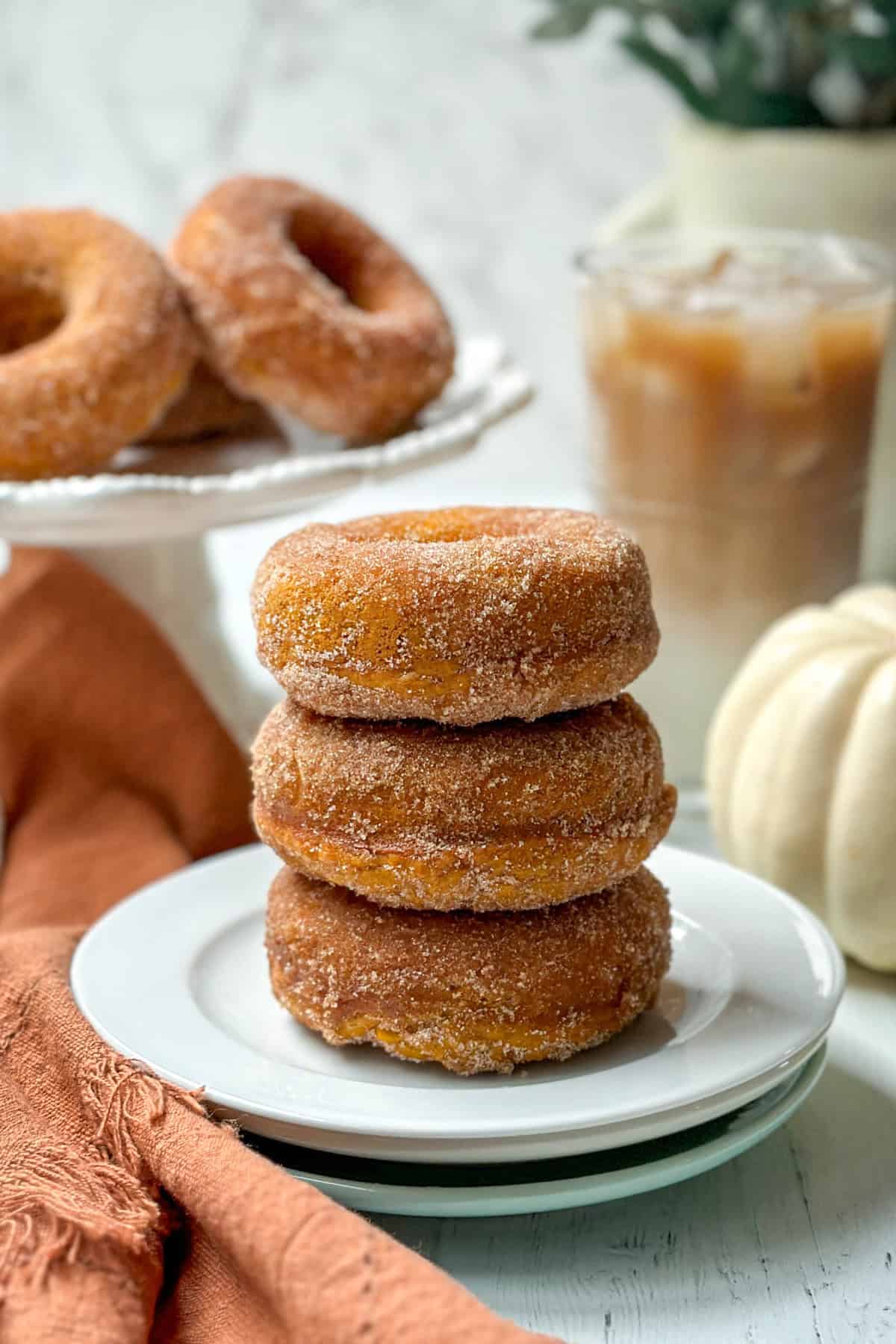 Stacked of baked pumpkin donuts on a plate with more in the background.