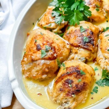 Golden-browned slow cooker chicken thighs in a creamy sauce, garnished with chopped parsley, served in a white oval dish.
