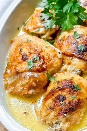 Golden-browned slow cooker chicken thighs in a creamy sauce, garnished with chopped parsley, served in a white oval dish.