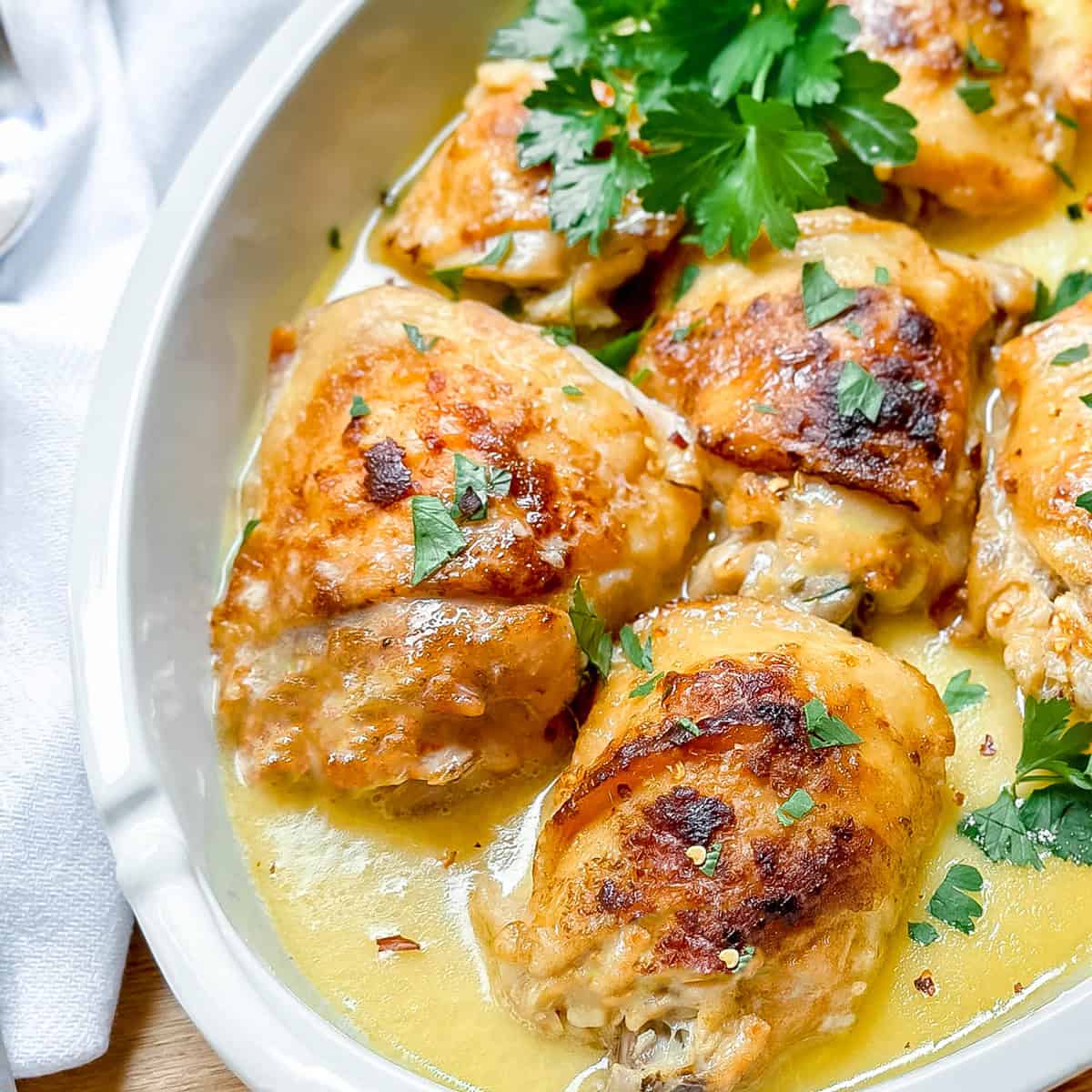 Golden-browned slow cooker chicken thighs in a creamy sauce, garnished with chopped parsley, served in a white oval dish.