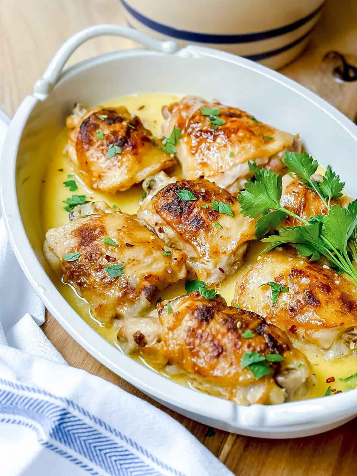 Slow Cooker chicken thighs topped with parsley, served in a white oval dish with a creamy sauce.