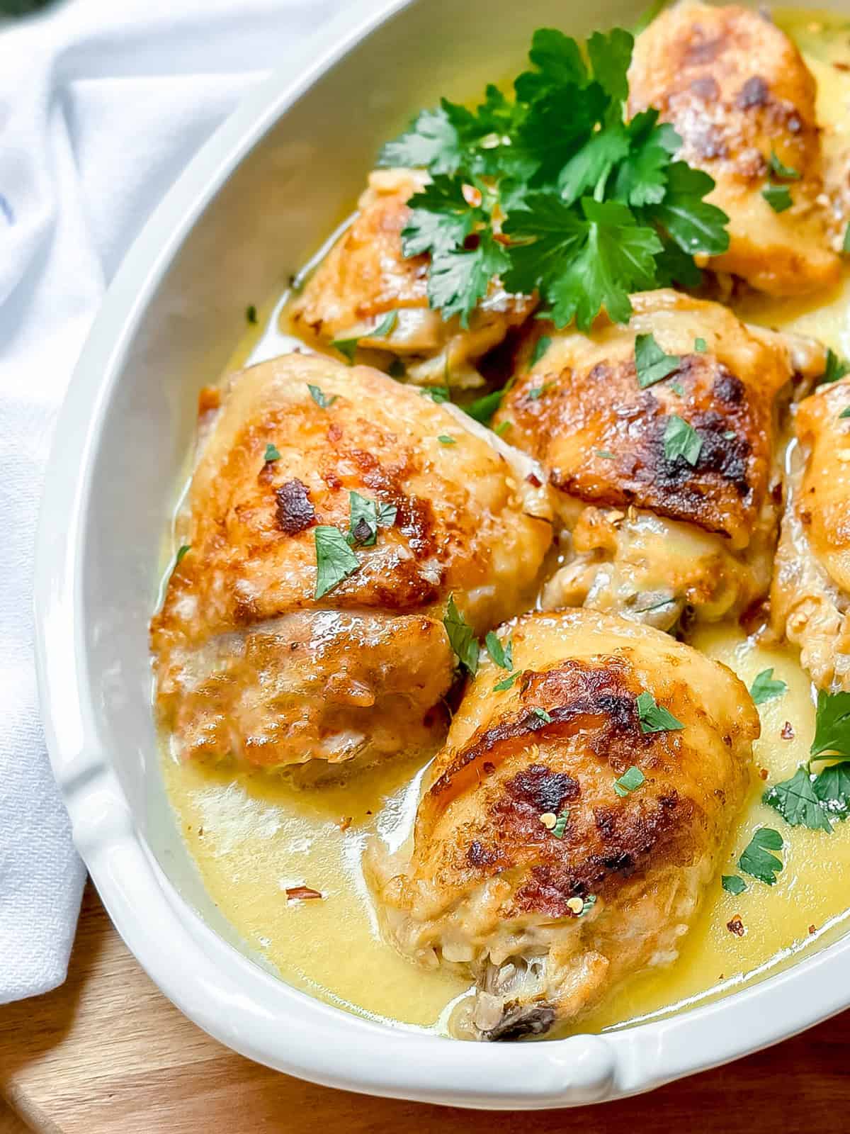 Golden-brown baked slow cooker chicken thighs in a creamy sauce, garnished with chopped parsley, served in a white dish.