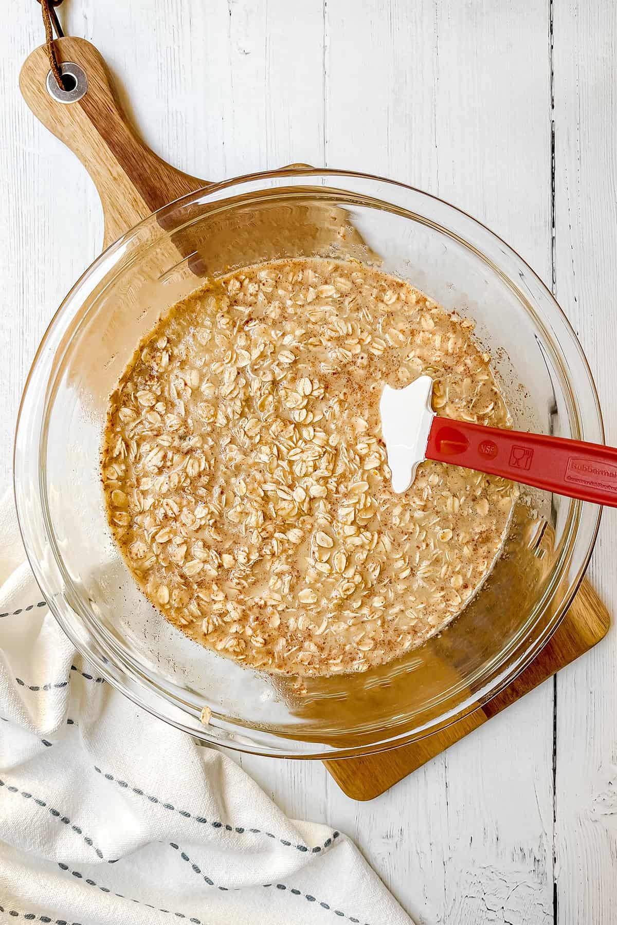 Rolled oats mixed with milk, eggs, honey, and cinnamon in a glass mixing bowl with a red spatula, forming batter for baked oatmeal cups.