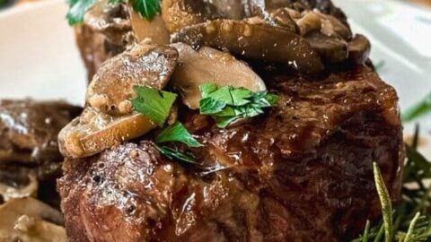Side view of Grilled Steak with Mushroom Sauce and freshly chopped parsley on a wooden board for serving