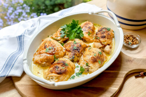 Side view of Slow Cooker Chicken Thighs in a white oval casserole with fresh parsley and garlic coconut sauce