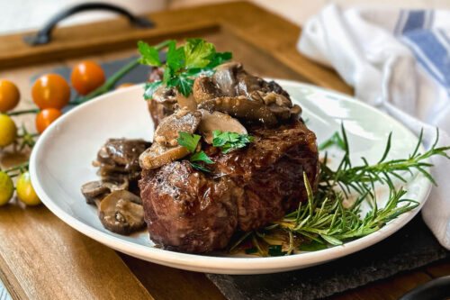 Side view of Grilled Steak with Mushroom Sauce and freshly chopped parsley on a wooden board for serving