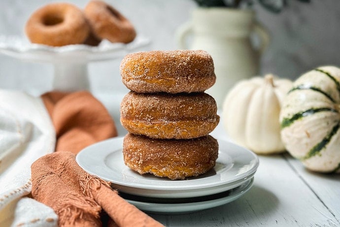 Side view of stacked pumpkin donuts on a white plate with more in the background