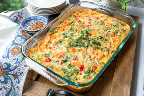Closeup top view of Sweet Potato Breakfast Casserole with fresh parsley and red pepper flakes on a wooden cutting board