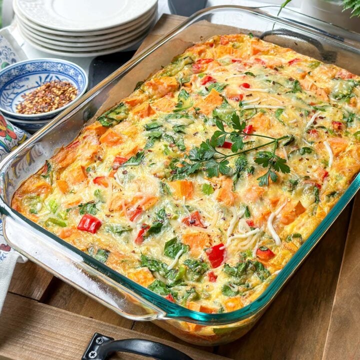 Closeup top view of Sweet Potato Breakfast Casserole with fresh parsley and red pepper flakes on a wooden cutting board