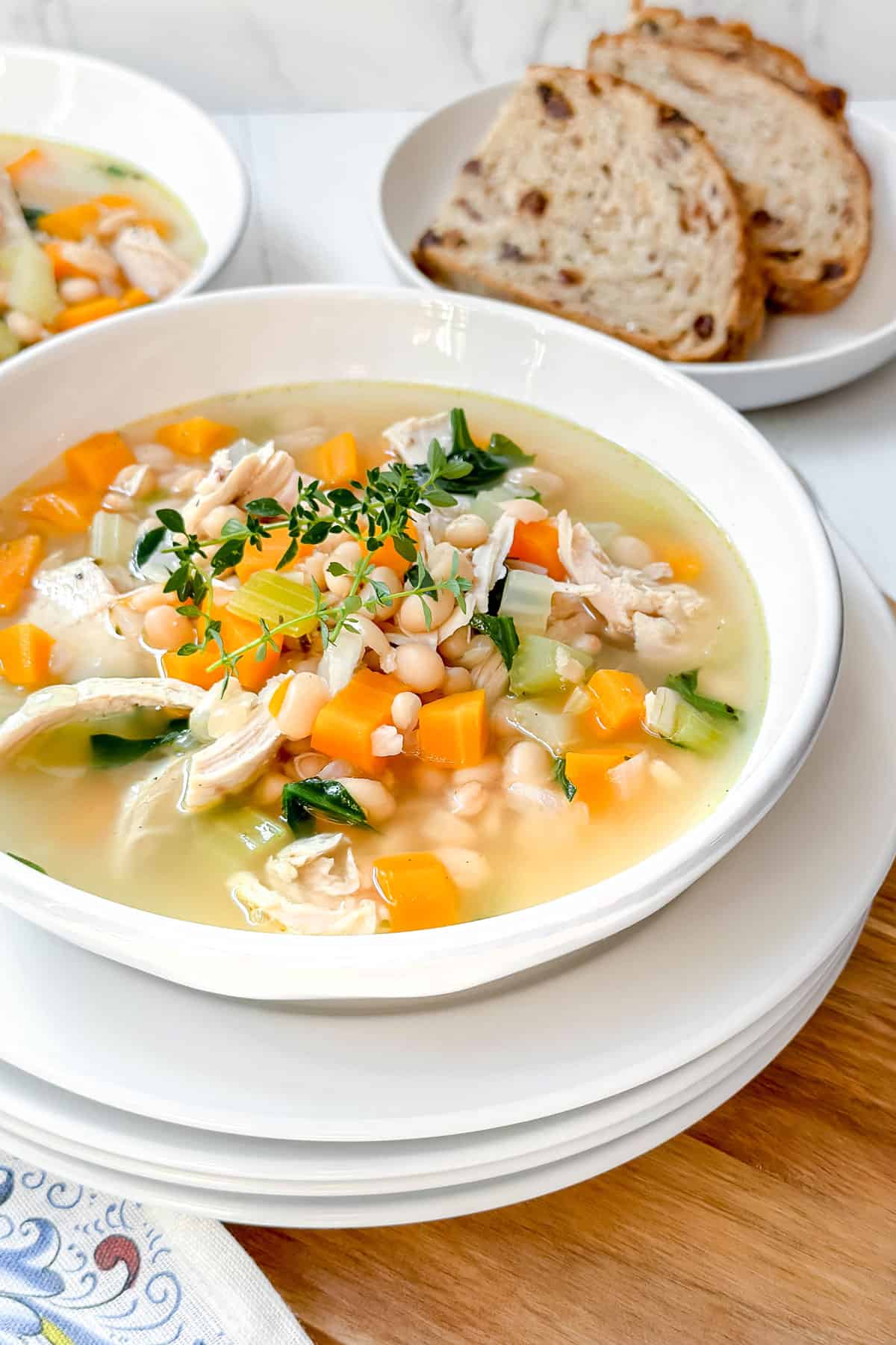 Chicken and White Bean Soup ladeled into a white bowl and topped with fresh thyme with whole grain bread in the background.