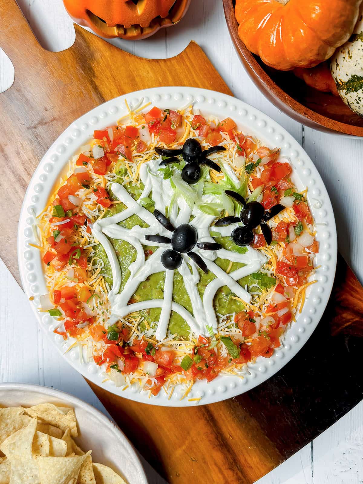 Halloween 7 Layer Dip topped with a sour cream spiderweb and black olive spiders.