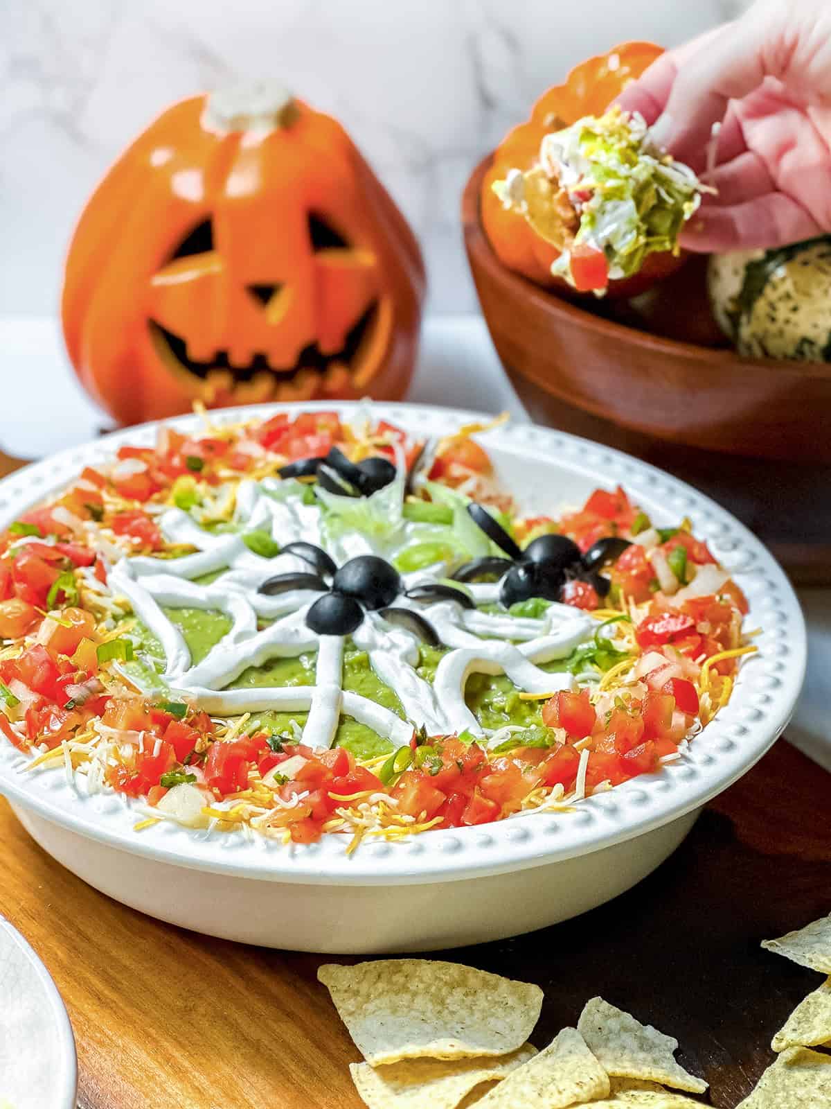 Tortilla chip scooping Halloween 7 Layer Dip topped with sour cream spiderweb and olive spiders.