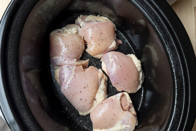 Top view of uncooked chicken thighs in a black slow cooker insert