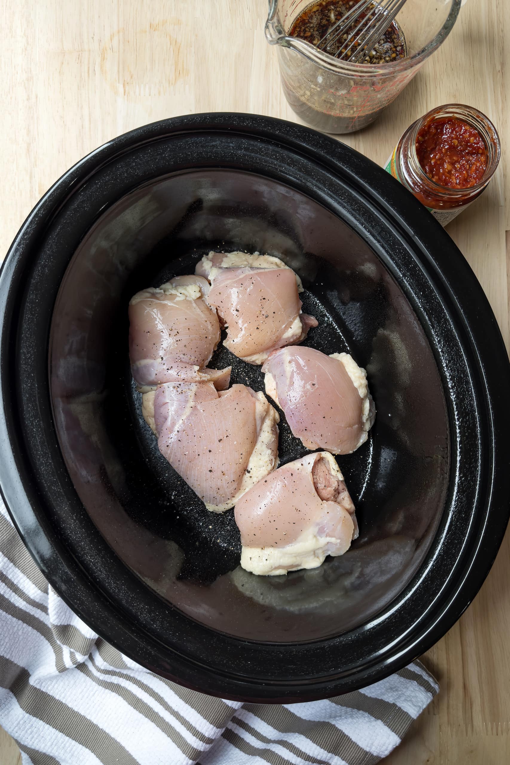 Top view of uncooked chicken thighs in a black slow cooker insert