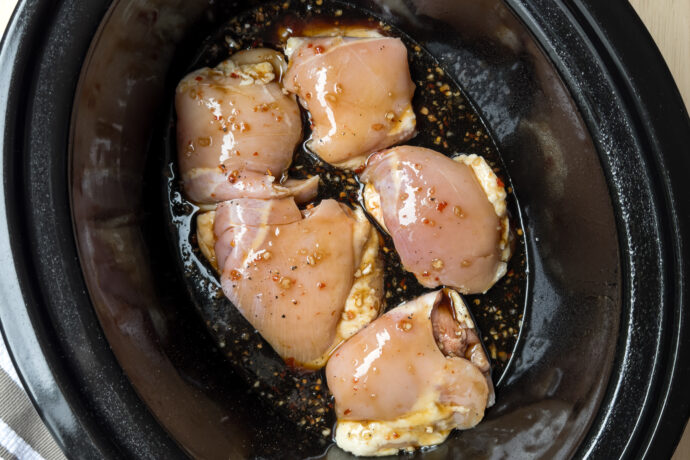 Top view of uncooked chicken thighs with honey garlic sauce in a black slow cooker