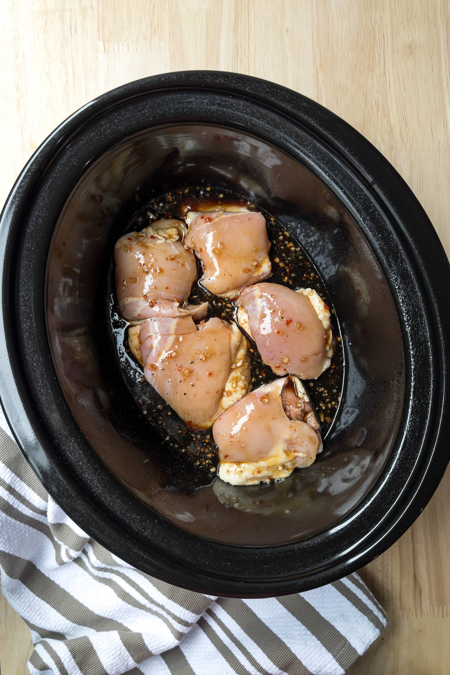 Top view of uncooked chicken thighs with honey garlic sauce in a black slow cooker