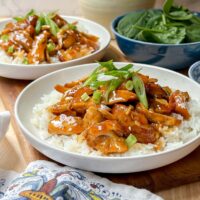 Closeup side view of Slow Cooker Honey Garlic Chicken over rice with spinach in the background