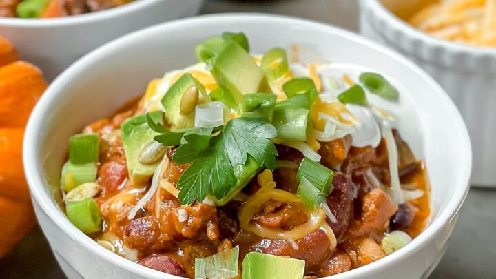 Closeup view of Pumpkin Turkey Chili in a white bowl with parsley, avocado and shredded cheese