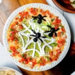 Top view of 10 minute Halloween 7 Layer Dip with tortillas on the side and olive spiders.