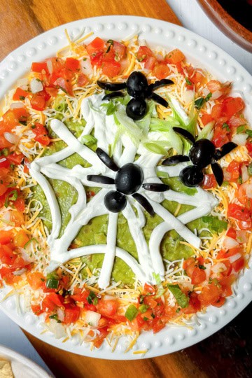 Top view of 10 minute Halloween 7 Layer Dip with tortillas on the side and olive spiders.
