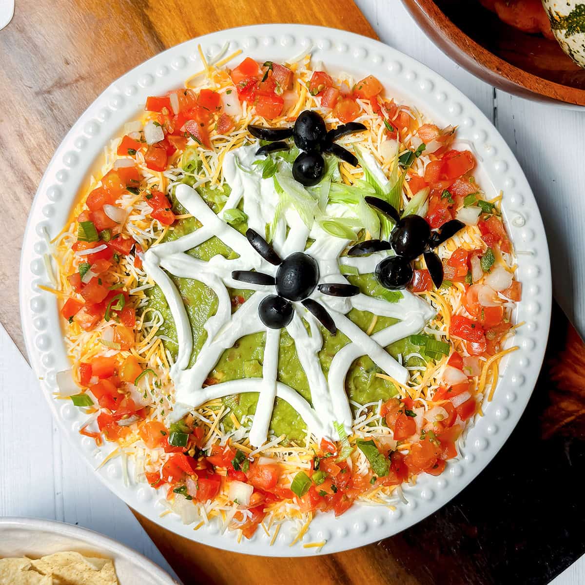 Top view of 10 minute Halloween 7 Layer Dip with tortillas on the side and olive spiders.